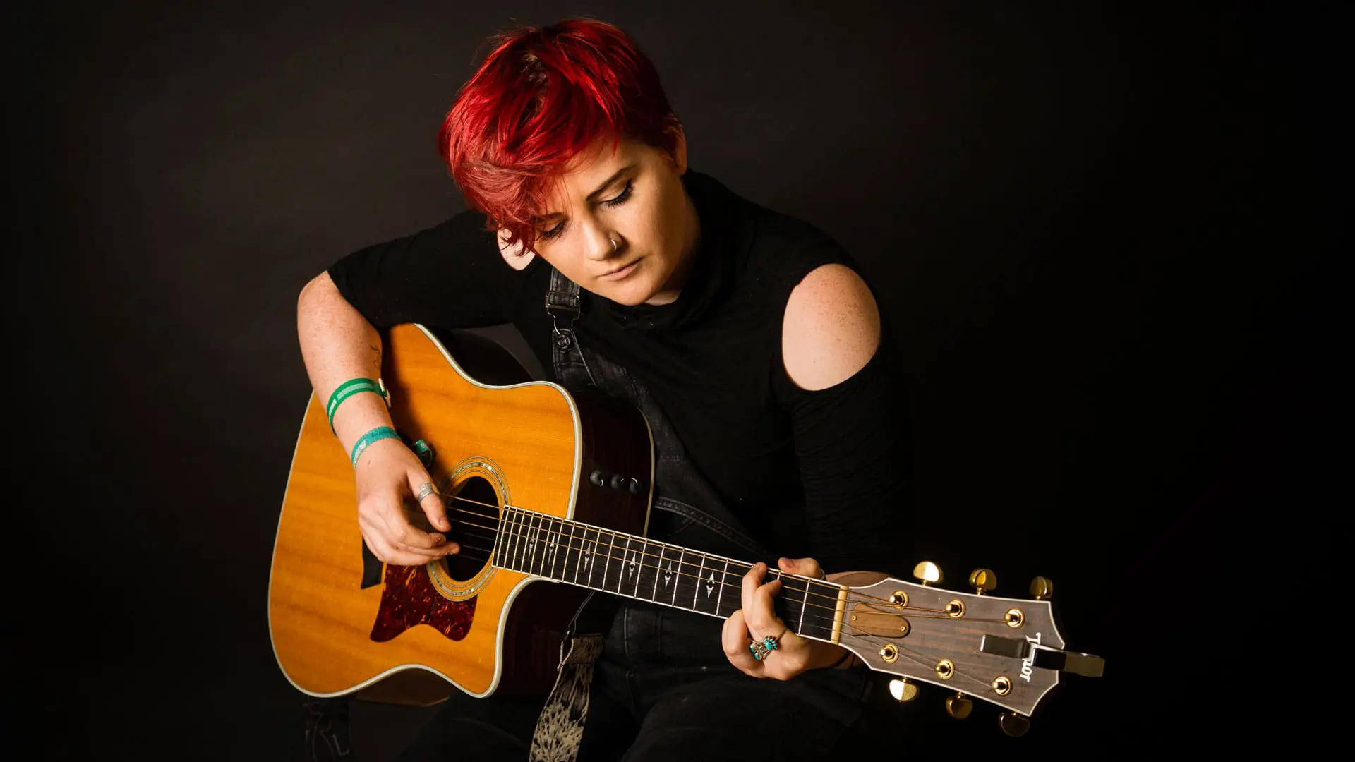 Person playing acoustic guitar against dark background.