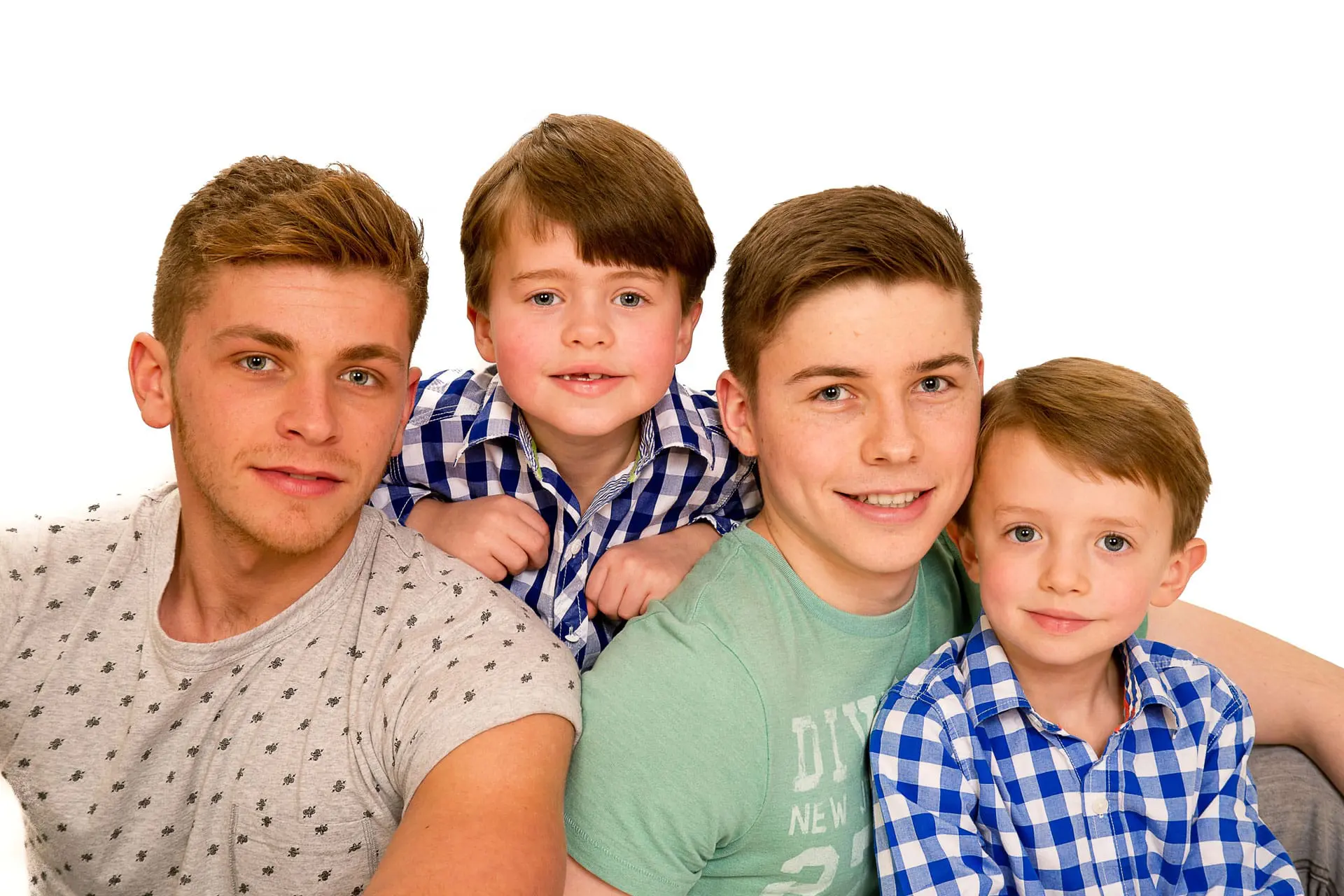 Four young boys smiling together, wearing casual clothing.