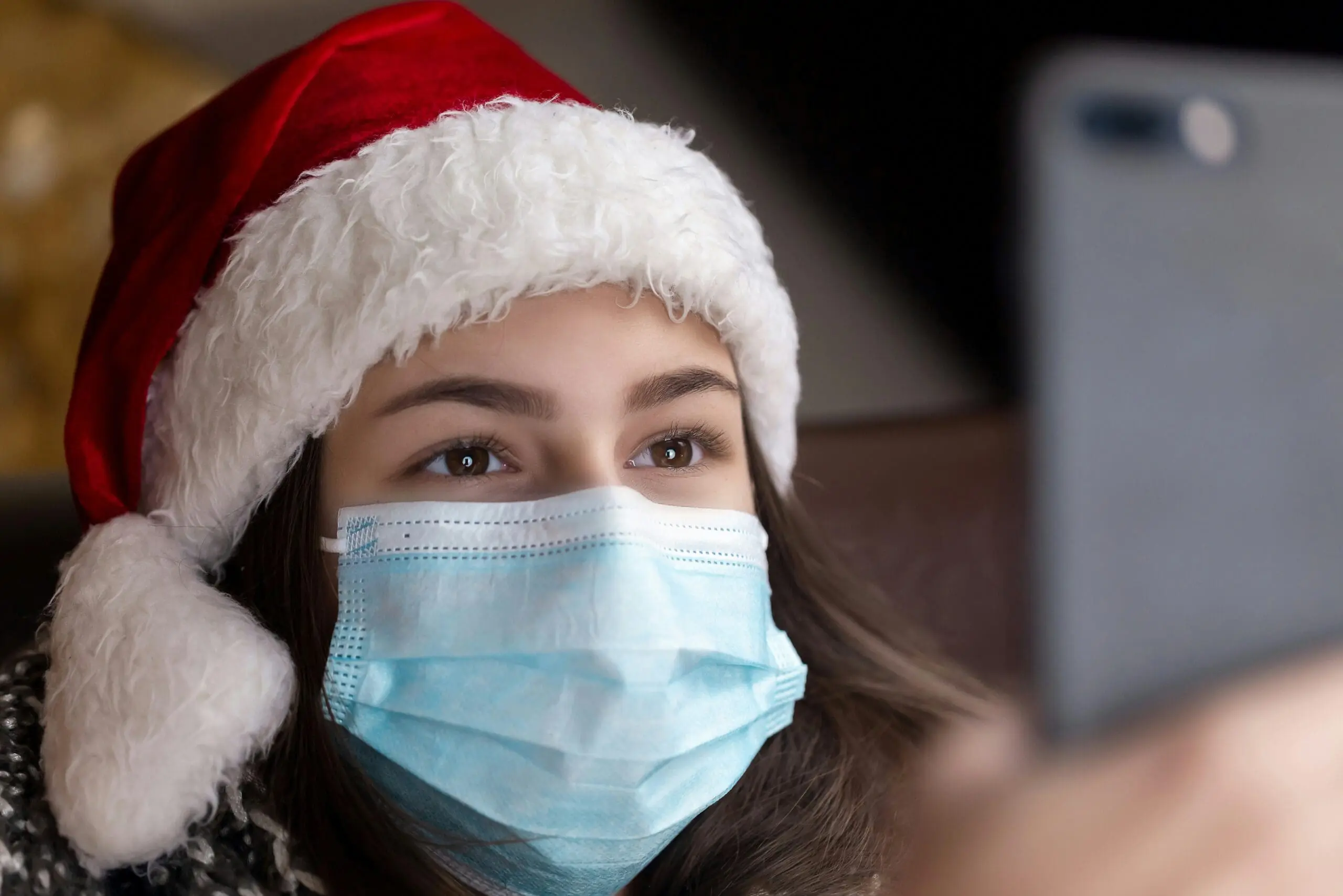Person in Santa hat, wearing face mask, taking selfie.