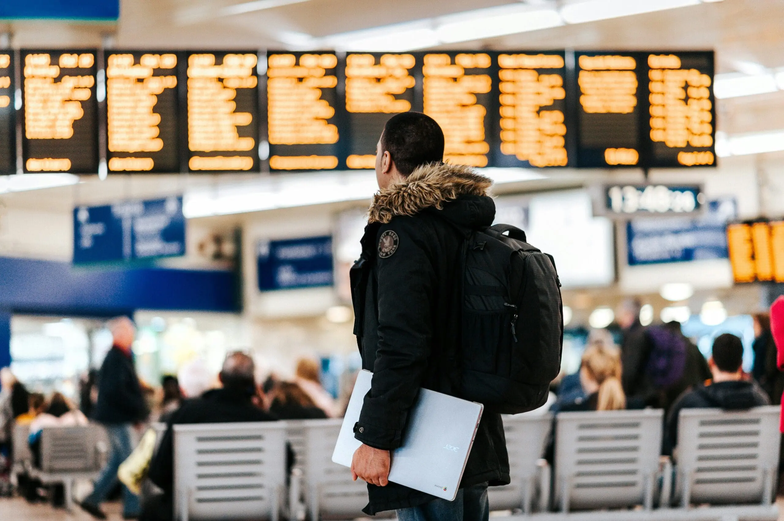 Traveller checking departure board at busy station.